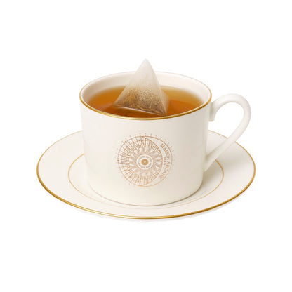 Tasse à thé en porcelaine de Chine Maison Arcane avec sa soucoupe ornée de dorure élégante, infusette de thé en train d'infuser dans la tasse.